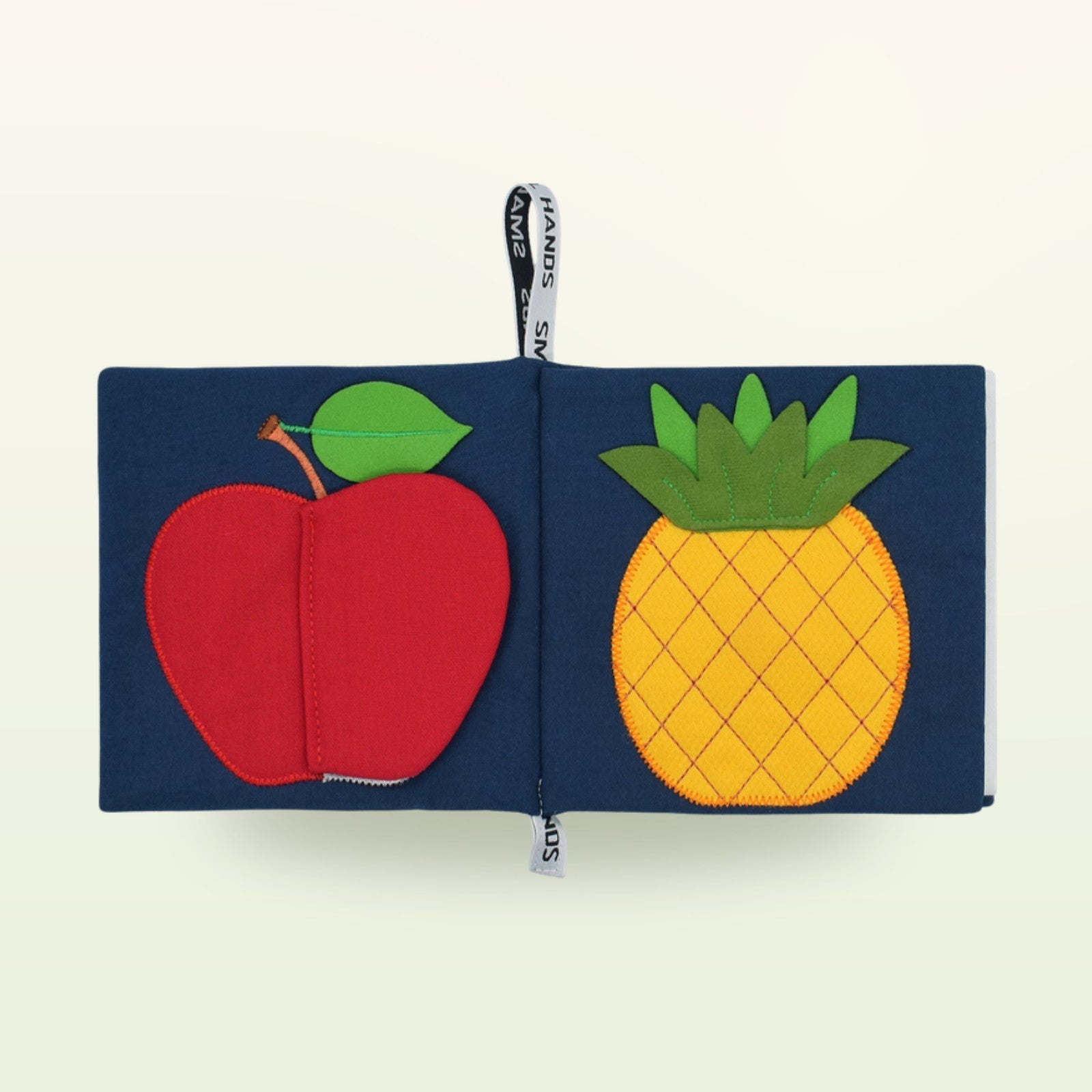 Small Hands Exotische Früchte Montessori Stoffbuch aufgeschlagen – Apfel und Ananas auf sanftem Creme-Hintergrund – ab 0 Monaten